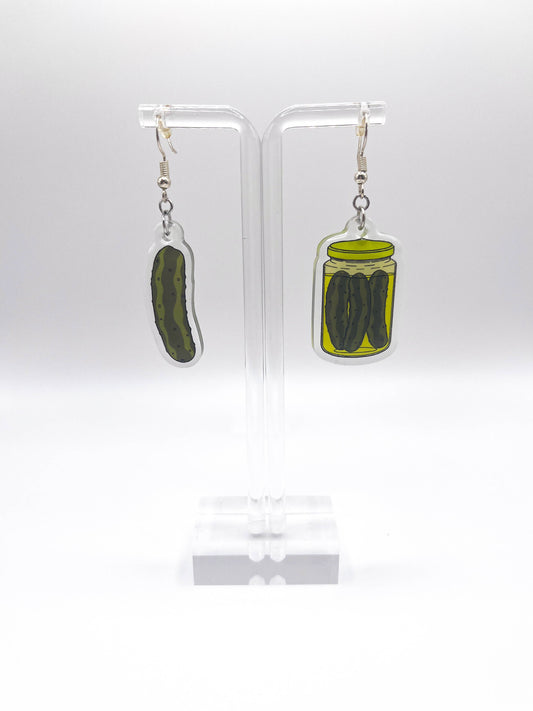 Pickle-themed earrings on clear stands against a white background