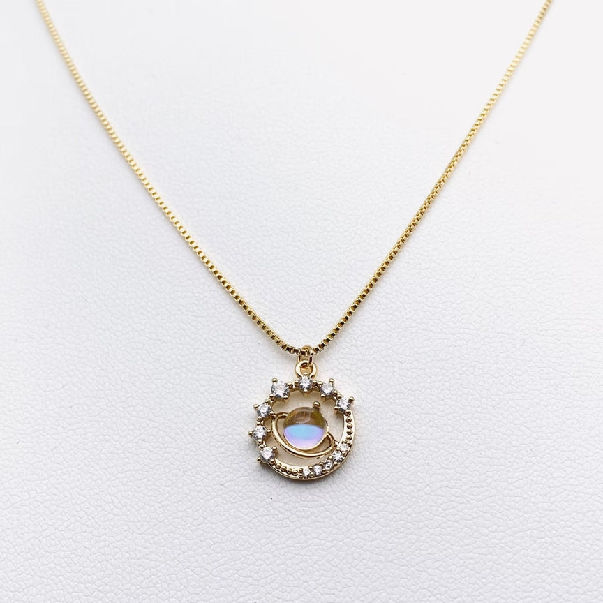 The 14k gold plated zircon inlaid planet necklace by faire, featuring a circular pendant with cubic zirconia and a mother-of-pearl inlay on its textured surface, shines beautifully against the white background.
