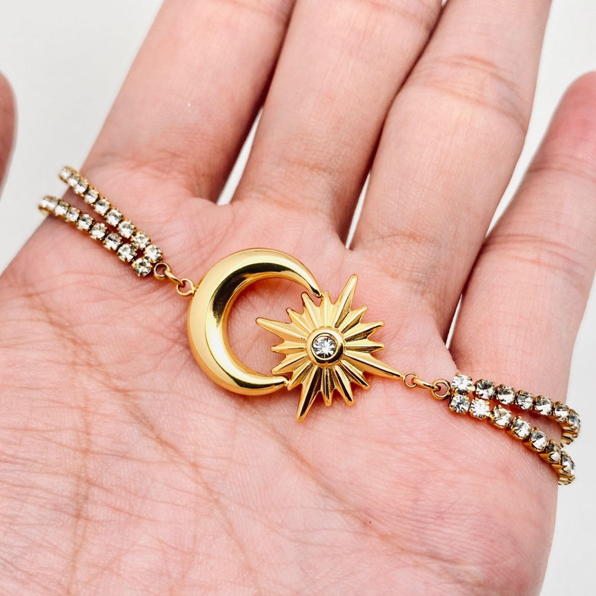 A hand holding the 18k gold plated Star Moon charm cubic zirconia bracelet by faire, featuring a gold crescent moon and star design. This bracelet, crafted with stainless steel and adorned with sparkling cubic zirconia accents along the band, adds a touch of elegance to this celestial-themed piece.