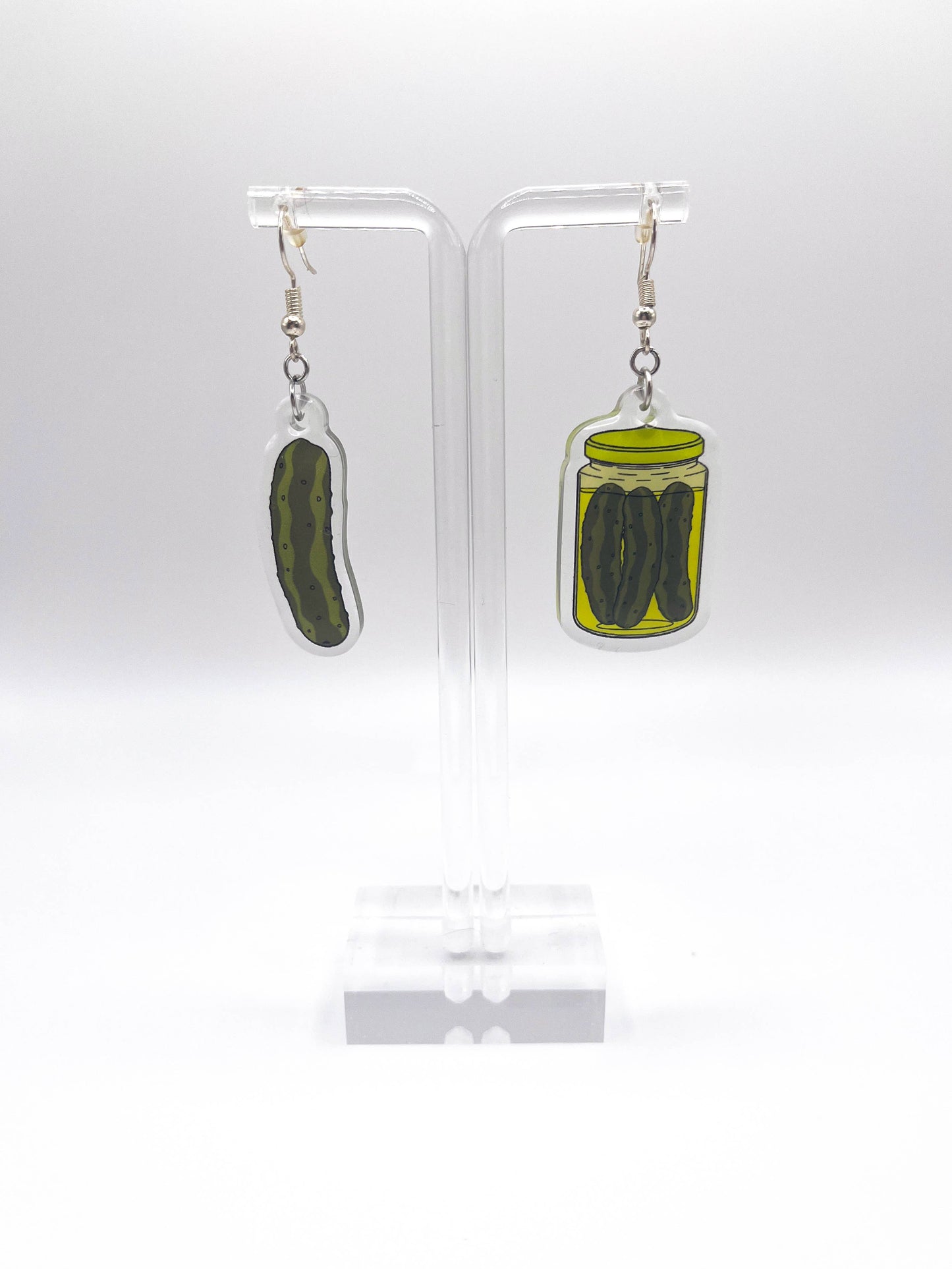 Pickle-themed earrings on clear stands against a white background