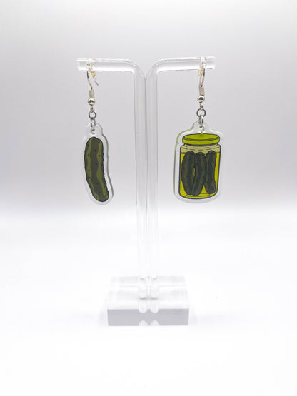 Pickle-themed earrings on clear stands against a white background