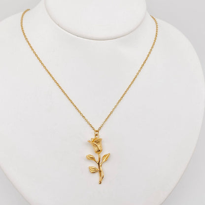 The 18K gold plated Rose pendant necklace by faire is a delicate piece featuring a pendant shaped like a blooming rose with leaves. It is crafted with vacuum electroplating and displayed on a white stand, showcasing its elegant design and intricate details.