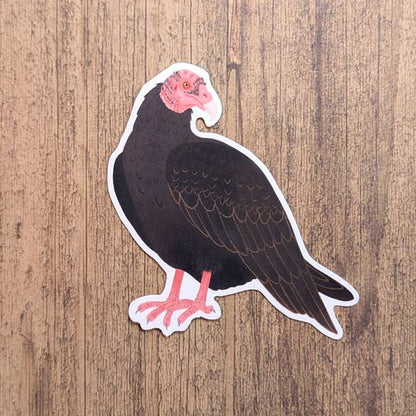 Sticker of a turkey vulture with a pink face and feet on a wooden background