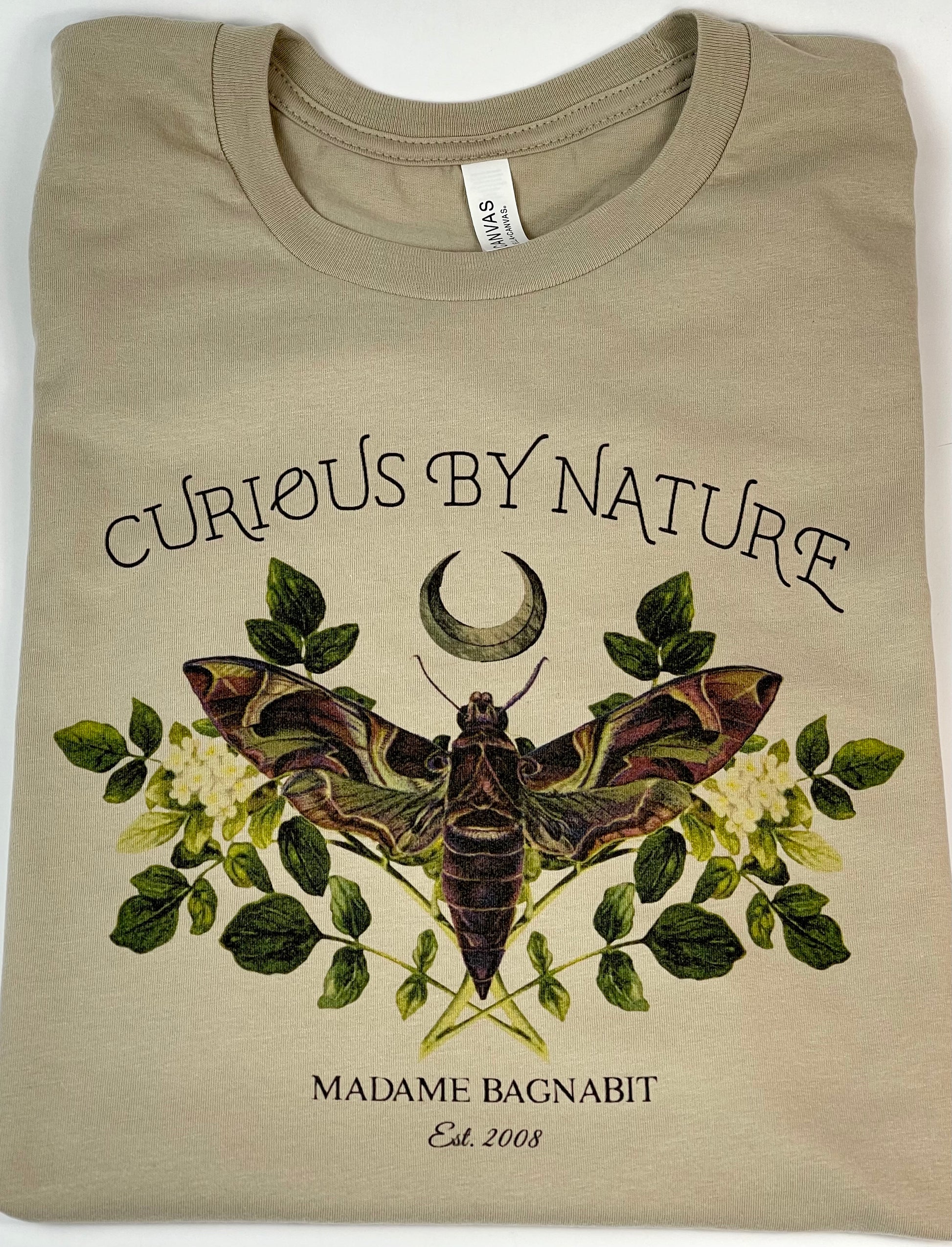 Beige t-shirt with moth and floral design, text 'Curious by Nature' and 'Madame Bagnavit' on a white background