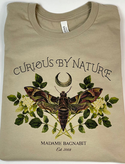 Beige t-shirt with moth and floral design, text 'Curious by Nature' and 'Madame Bagnavit' on a white background