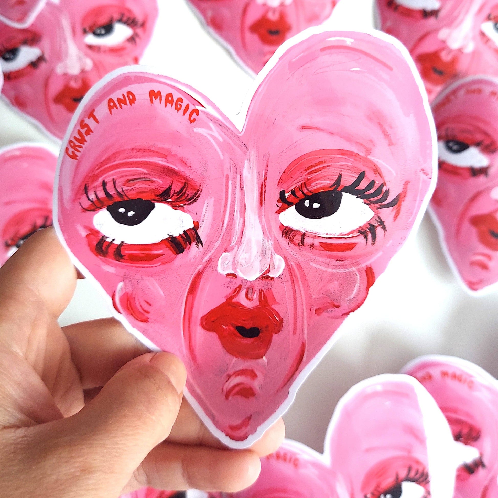 Pink face-shaped stickers with artistic designs held by a hand against a white background.