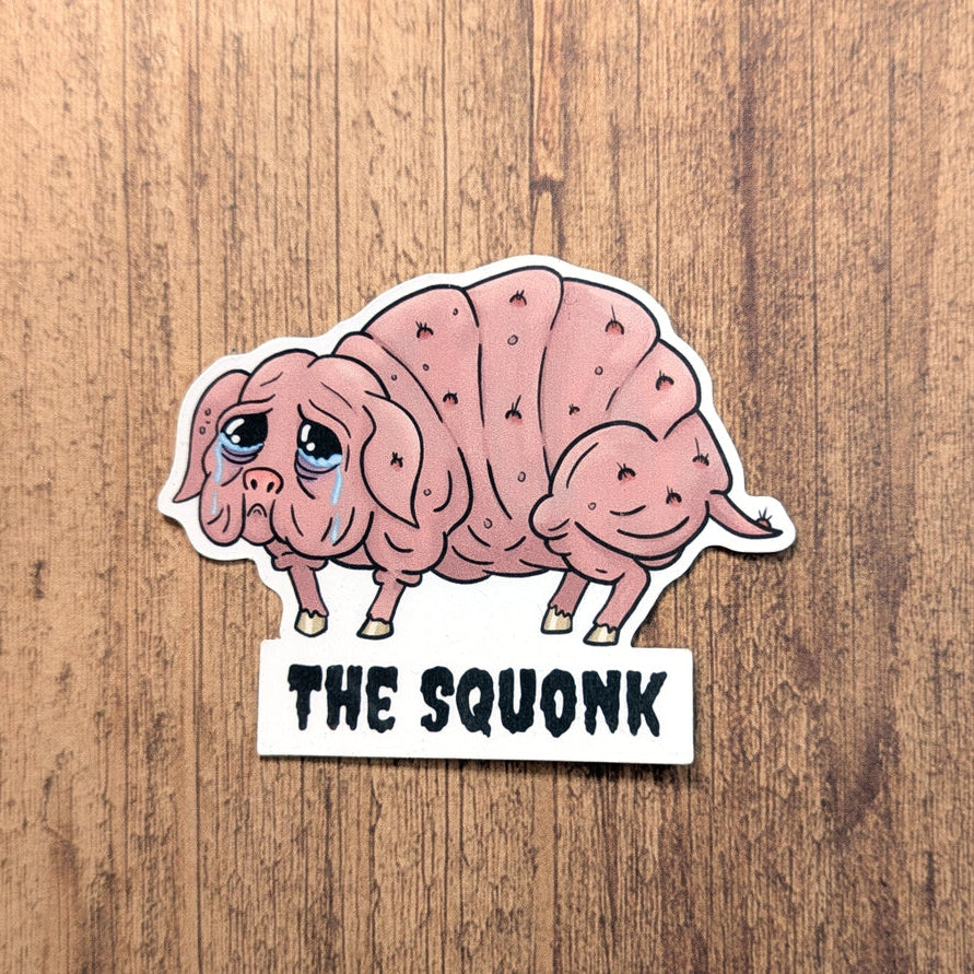 Sticker of a pink creature labeled 'The Squonk' on a wooden background