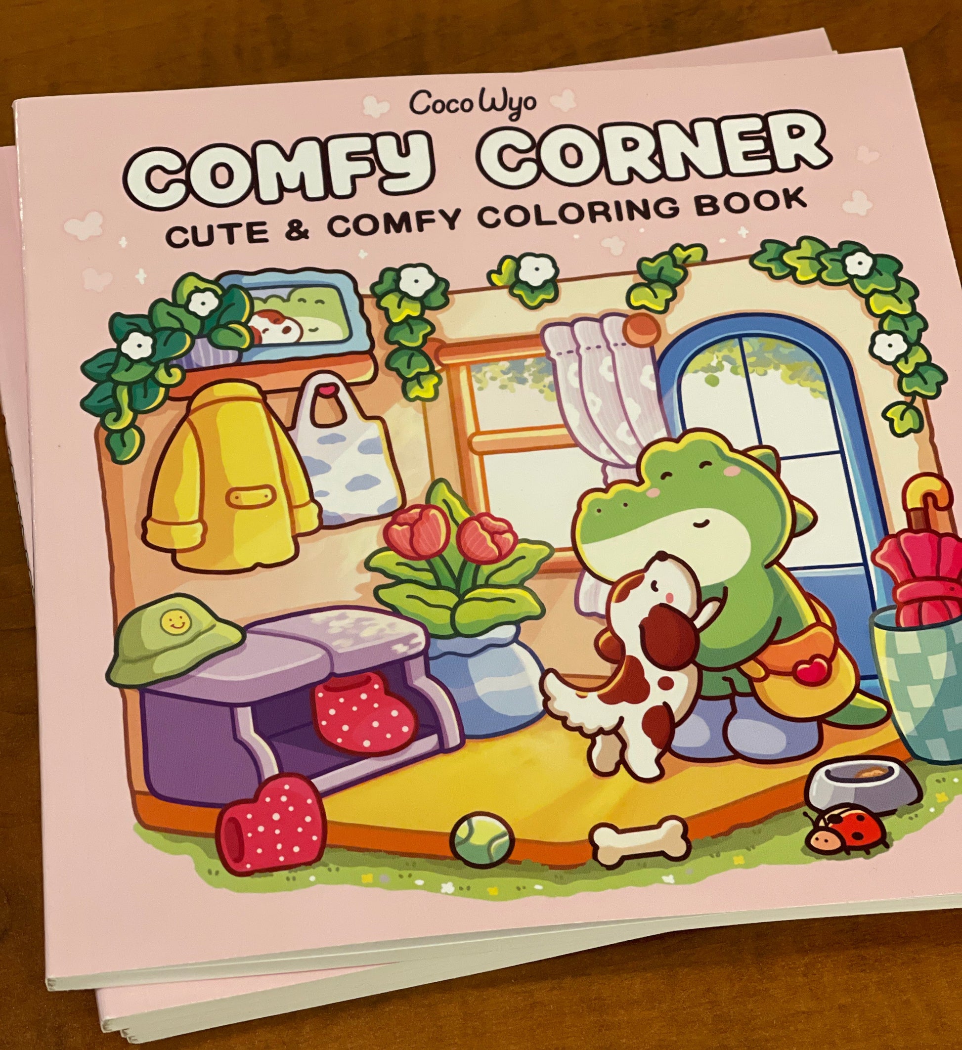 Coloring book titled 'Comfy Corner' with a cartoon dog on the cover, on a wooden surface.