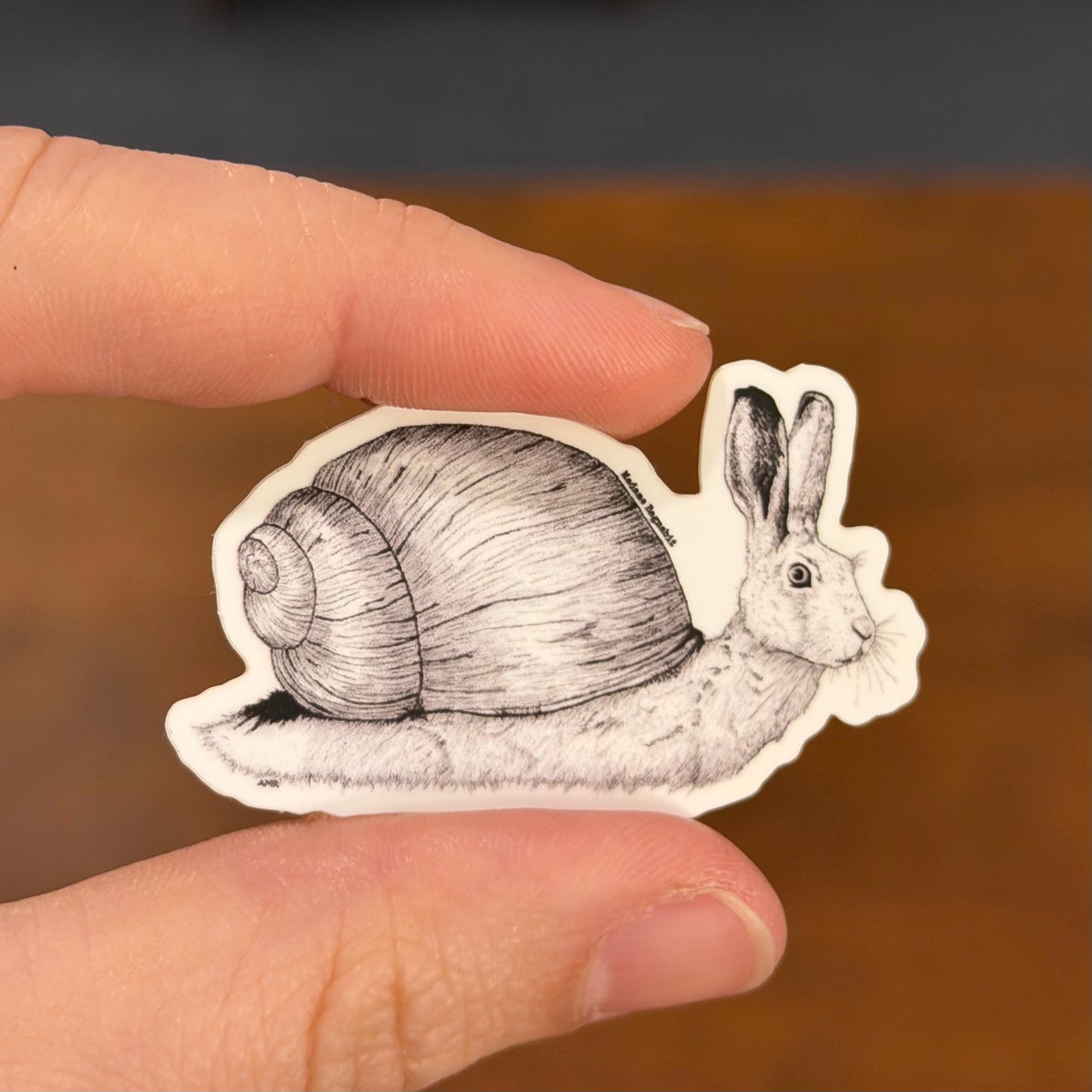 Hand holding a sticker of a rabbit with a snail shell against a blurred background
