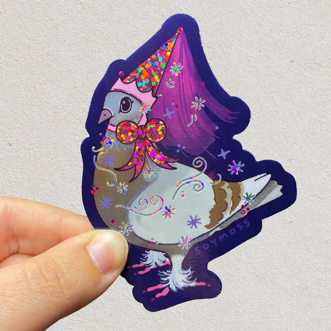 Colorful sticker of a pigeon with a purple hat held by a hand on a light gray background