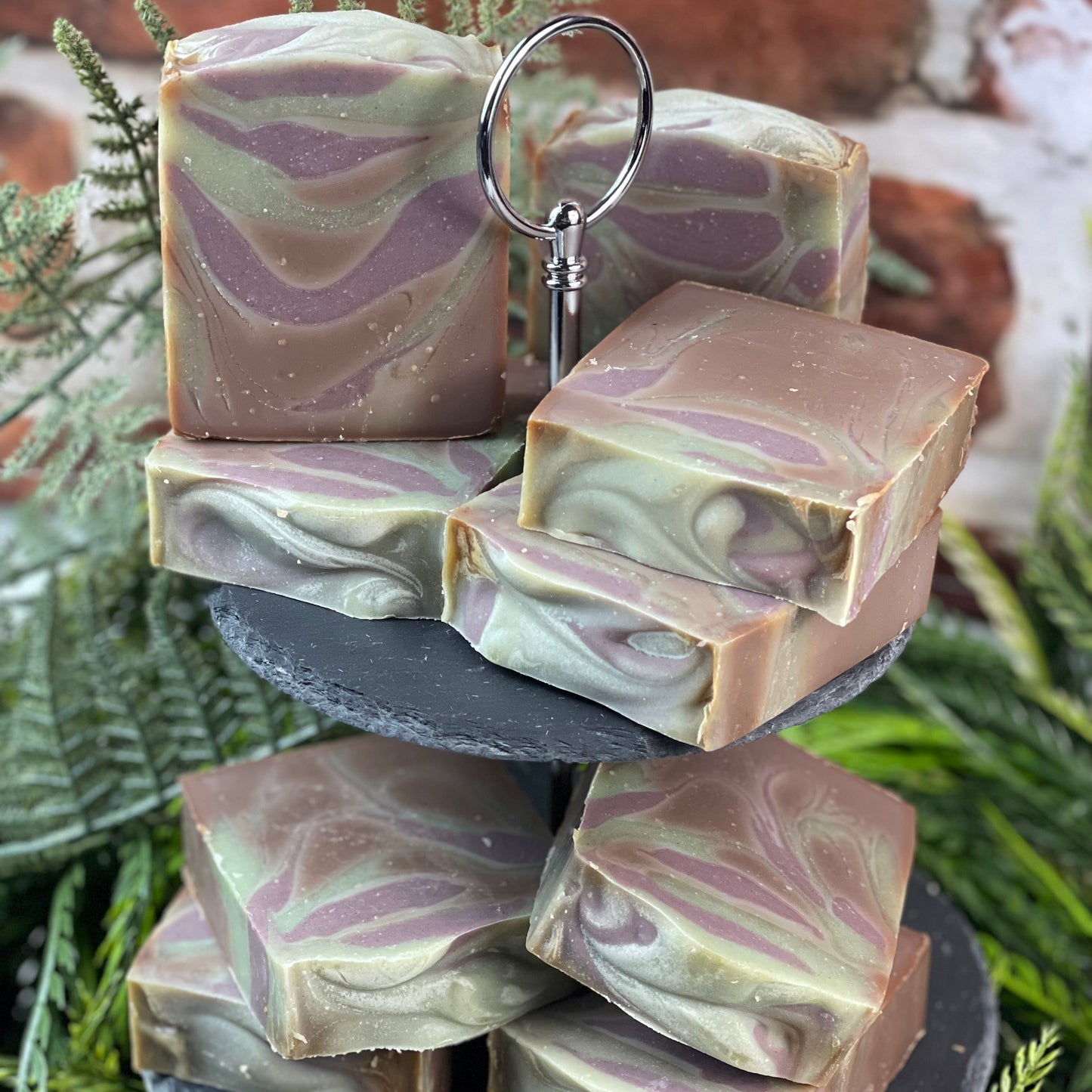 Stack of marbled soap bars on a tiered stand with greenery in the background