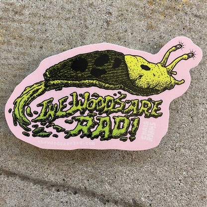 Sticker with a slug illustration and text 'The Woods Are Rad!' on a concrete surface