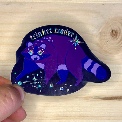 holographic sticker with raccoon that says trinket trader