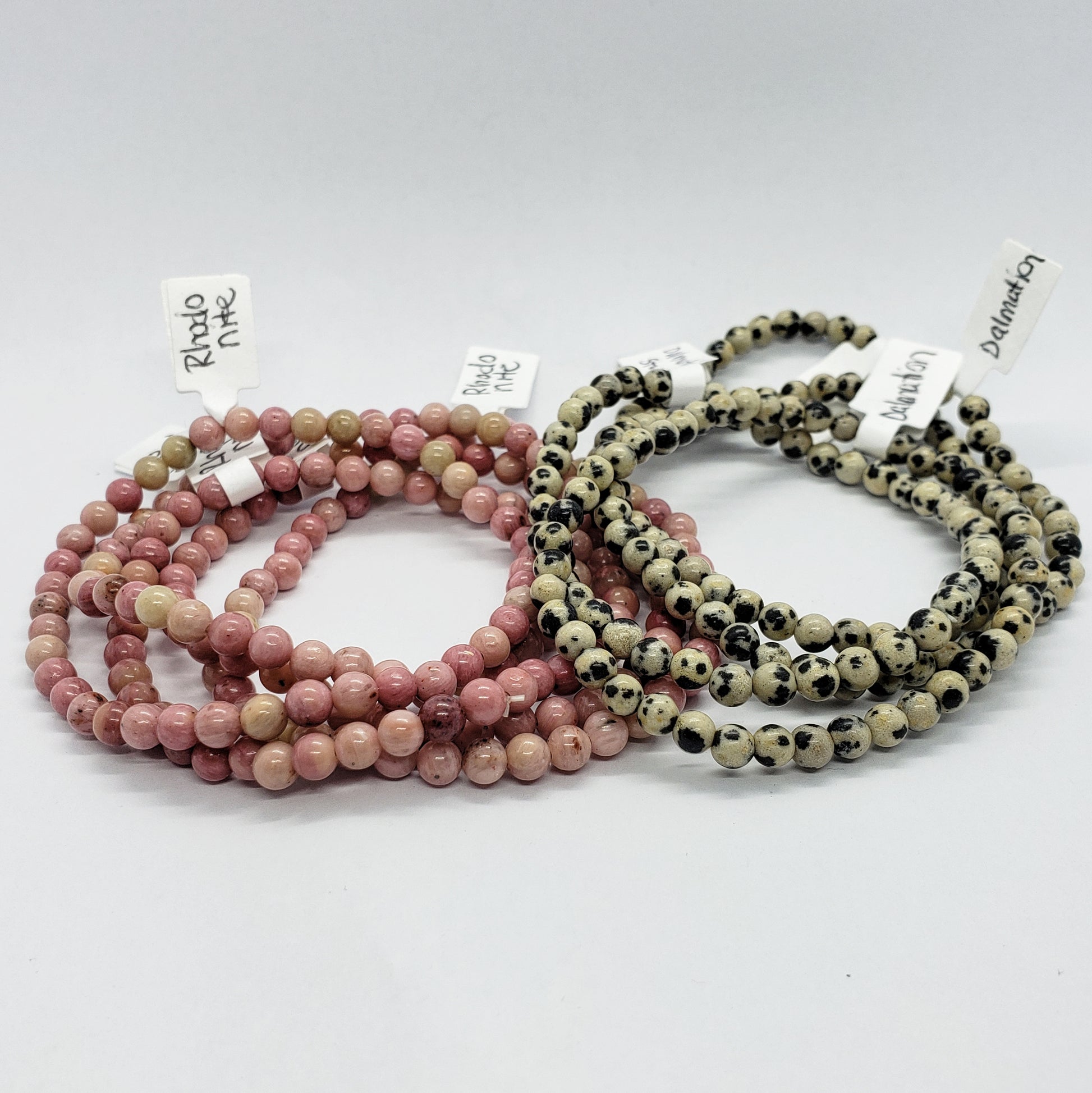 Introducing the 4mm Energy Stone Bracelets by Madame Bagnabit: a beautiful pair featuring one set with light pink rhodochrosite beads and another with speckled dalmatian jasper beads. Each set comes with labels identifying the type of stone used, all elegantly displayed on a white background.