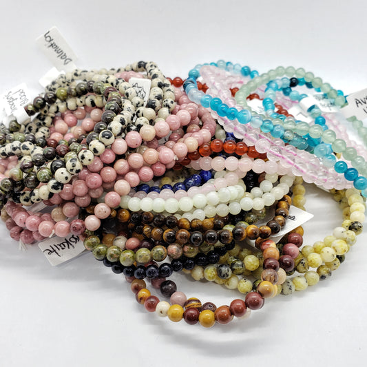 A pile of Madame Bagnabit's 4mm Energy Stone Bracelets is beautifully displayed, showcasing an array of natural stone bracelets with vibrant beads in shades of pink, blue, brown, and white, some adorned with striking marbled patterns. Each bracelet includes a small attached tag.